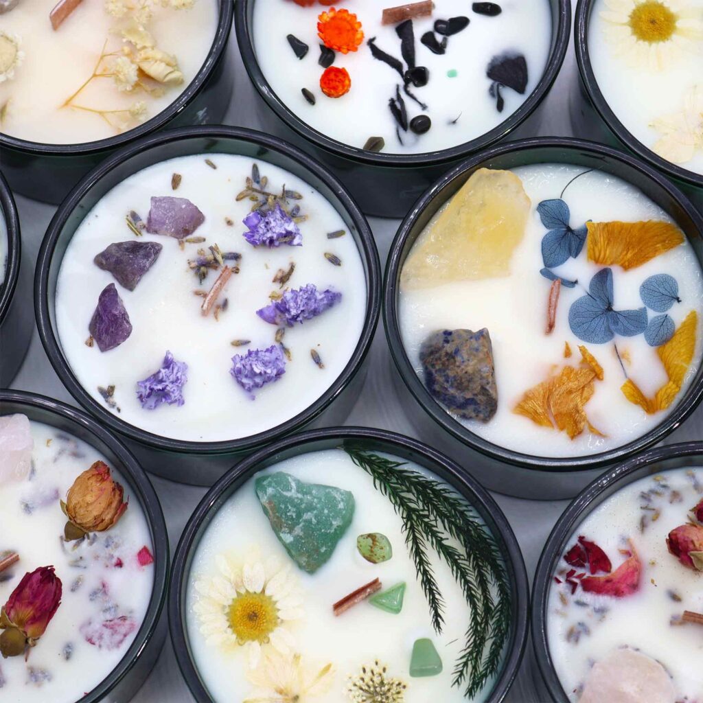 Top-down view of handmade candles in black tins, embedded with dried flowers, herbs, and crystals